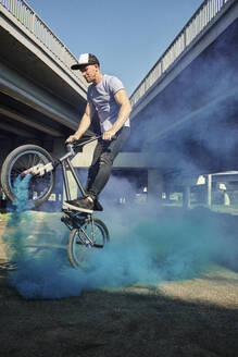 Mann macht Stunt mit BMX-Rad und stößt in der Nähe einer Brücke blauen Rauch aus - MRPF00052