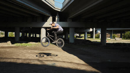 Man jumping with BMX bike near bridge - MRPF00054