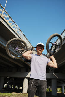 Mann trägt BMX-Rad über Schultern in der Nähe der Brücke - MRPF00055