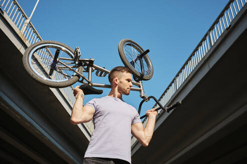 Mann trägt BMX-Rad auf den Schultern in der Nähe von Brücke unter Himmel - MRPF00056