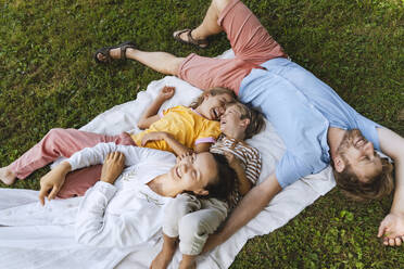 Happy family lying down on blanket at park - NDEF01397