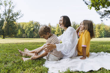 Happy woman with son and daughter sitting on blanket at park - NDEF01400