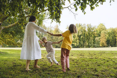 Mutter hält die Hände von Sohn und Tochter, die im Park spielen - NDEF01433