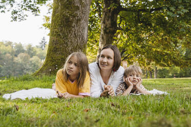 Mother lying down with son and daughter on grass at park - NDEF01436