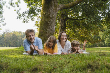 Familie liegt zusammen auf dem Rasen im Park - NDEF01437