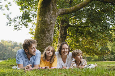 Father and mother lying down with children at park - NDEF01438