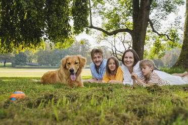 Glückliche Familie mit Hund im Gras liegend im Park - NDEF01439