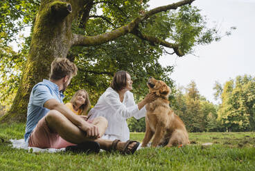 Family enjoying weekend with dog sitting on grass at park - NDEF01442