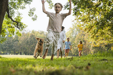 Playful boy running with dog and family on grass at park - NDEF01453