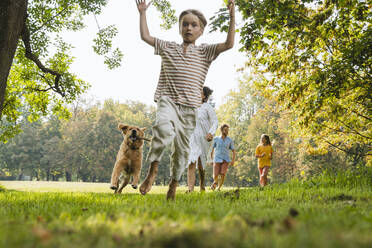 Verspielter Junge, der mit Hund und Familie auf einer Wiese im Park läuft - NDEF01453