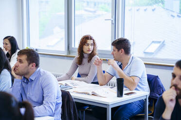 Diverse students discussing at desk in education training class - NJAF00630