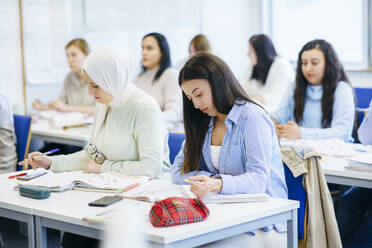 Multiethnische Freunde mit Büchern, die am Schreibtisch im Klassenzimmer lernen - NJAF00640