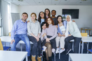 Lächelnde multiethnische Schüler, die sich im Klassenzimmer in den Armen liegen - NJAF00665
