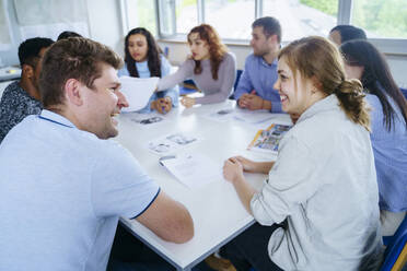 Fröhliche multiethnische Freunde sitzen am Schreibtisch in einem Schulungskurs - NJAF00675