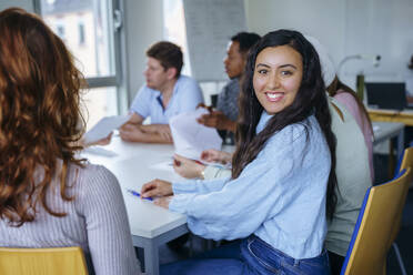 Smiling student sitting with multi-ethnic friends at desk in classroom - NJAF00679