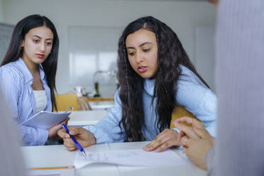 Woman with pen reading notes and explaining to friends in classroom - NJAF00680