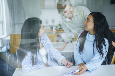 Smiling multi-ethnic students seen through glass in classroom - NJAF00682