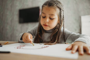 Girl with braided hair drawing with crayon at home - ANAF02401