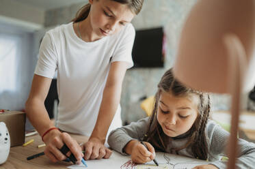 Girl assisting sister in drawing at home - ANAF02403