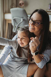 Smiling mother and daughter playing rock paper scissors at home - ANAF02409