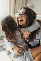 Mother embracing daughter and laughing at home - ANAF02411