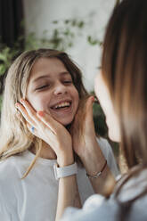 Mother touching happy daughter's cheeks at home - ANAF02415