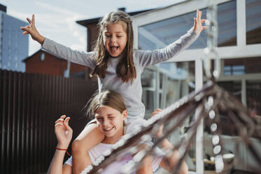 Lächelndes Mädchen, das seine Schwester auf den Schultern trägt, vor einem Haus - ANAF02417