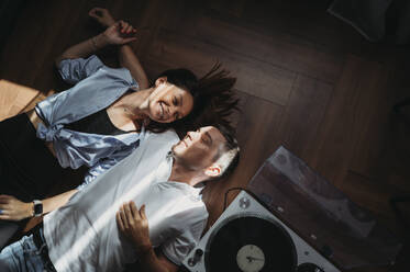 Smiling couple lying on floor near turntable at home - ANAF02429