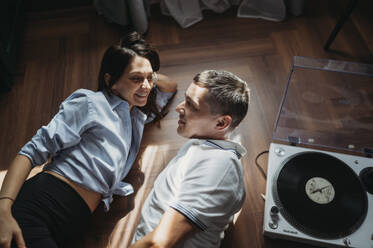 Smiling couple lying on floor and talking near turntable - ANAF02430