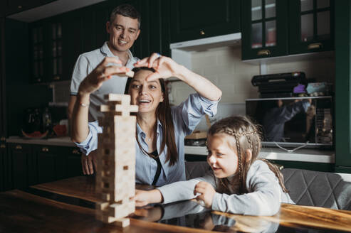 Happy family playing block removal game on table in kitchen - ANAF02436