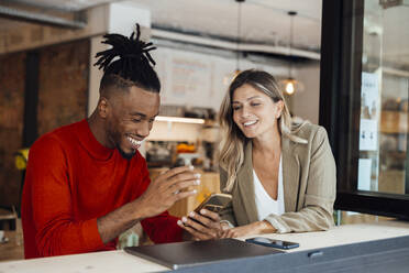 Glücklicher Kollege, der das Smartphone einer Geschäftsfrau im Café benutzt - JOSEF22092