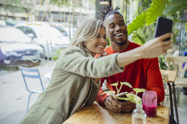 Businesswoman taking selfie with colleague through smart phone sitting at cafe - JOSEF22121