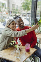 Business colleagues taking selfie through smart phone sitting at cafe - JOSEF22122