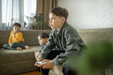 Boy playing video game with siblings at home - ANAF02445