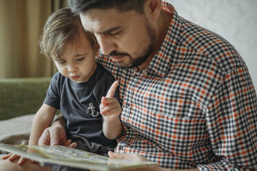 Father and son reading book together at home - ANAF02451