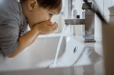 Junge wäscht Mund mit Wasser nach dem Zähneputzen im Badezimmer zu Hause - ANAF02453