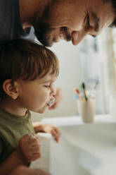 Father helping son to brush teeth in bathroom at home - ANAF02456