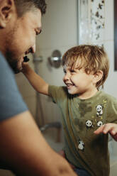 Playful boy brushing teeth of father in bathroom at home - ANAF02458
