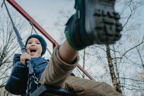 Fröhlicher Junge spielt auf einer Schaukel im Park unter dem Himmel - ANAF02460