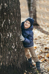 Smiling boy leaning on tree at park - ANAF02461