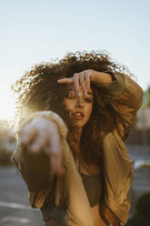 Young woman with curly hair dancing under sky - ANNF00658