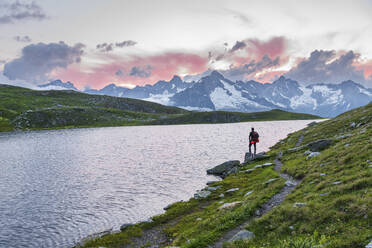 Hiker stands near the shore of Fenetre lake admiring the sunset over the massif of Mount Blanc, Ferret valley, Valais canton, Col du Grand-Saint-Bernard (St. Bernard mountain pass), Switzerland, Europe - RHPLF29065