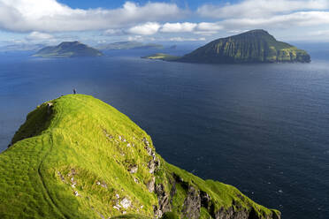 Hiker walks on top of a tall cliff overlooking the ocean, Nordradalur, Streymoy island, Faroe islands, Denmark, Europe - RHPLF29073