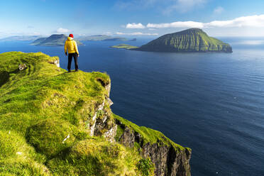 Hiker stands on top of a cliff admiring the rugged view, Nordradalur, Streymoy island, Faroe islands, Denmark, Europe - RHPLF29077