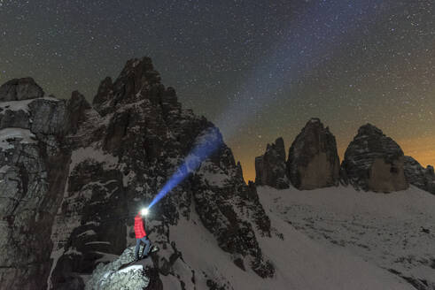 Man with head torch illuminates the starry sky over the snowy Paterno mountain and Tre Cime di Lavaredo (Lavaredo peaks), Sesto (Sexten), Dolomites, South Tyrol, Italy, Europe - RHPLF29081