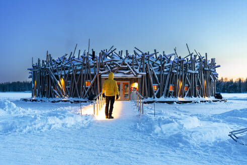 Person stands on the bridge connecting the main building of the illuminated Arctic Bath hotel made of logs, dusk time, Harads, Swedish Lapland, Norrbotten, Sweden, Scandinavia, Europe - RHPLF29083