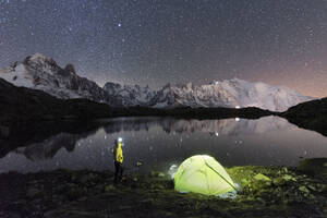 Person admiring the starry sky outside tent pitched on the shore of Cheserys lake surrounded by alpine landscape of Mont Blanc, Chamonix, Haute Savoie, French Alps, France, Europe - RHPLF29085