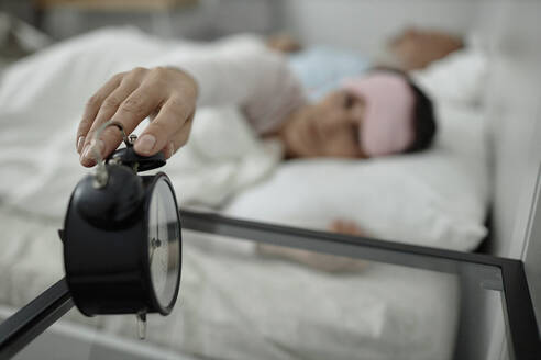 Woman turning off alarm clock while lying in bed - KPEF00343