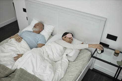 Frau schaltet den Wecker aus, während sie mit ihrem Mann im Bett liegt - KPEF00344