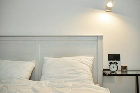 Interieur des Schlafzimmers, Bett mit weißer Bettwäsche und Nachttisch mit Wecker - KPEF00348
